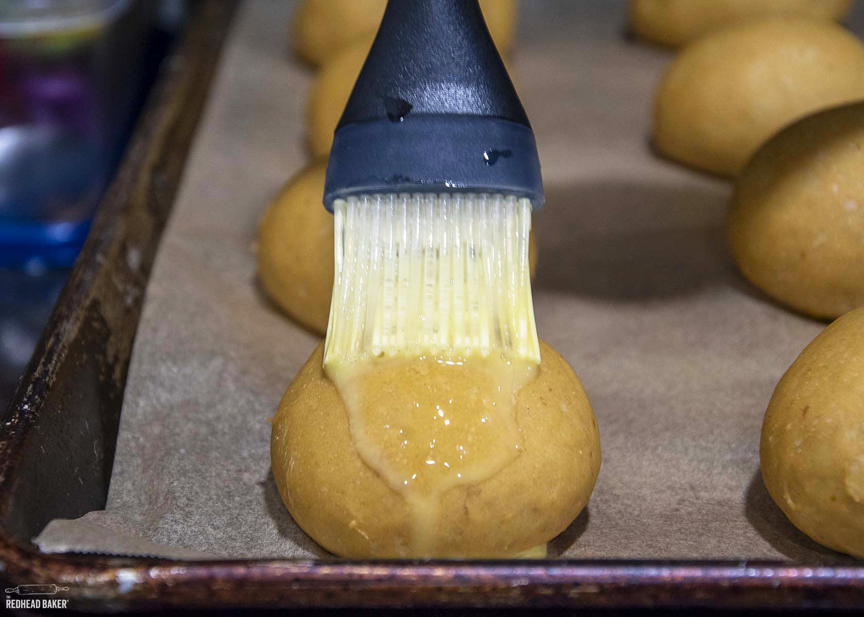 An unbaked roll being brushed with egg wash.