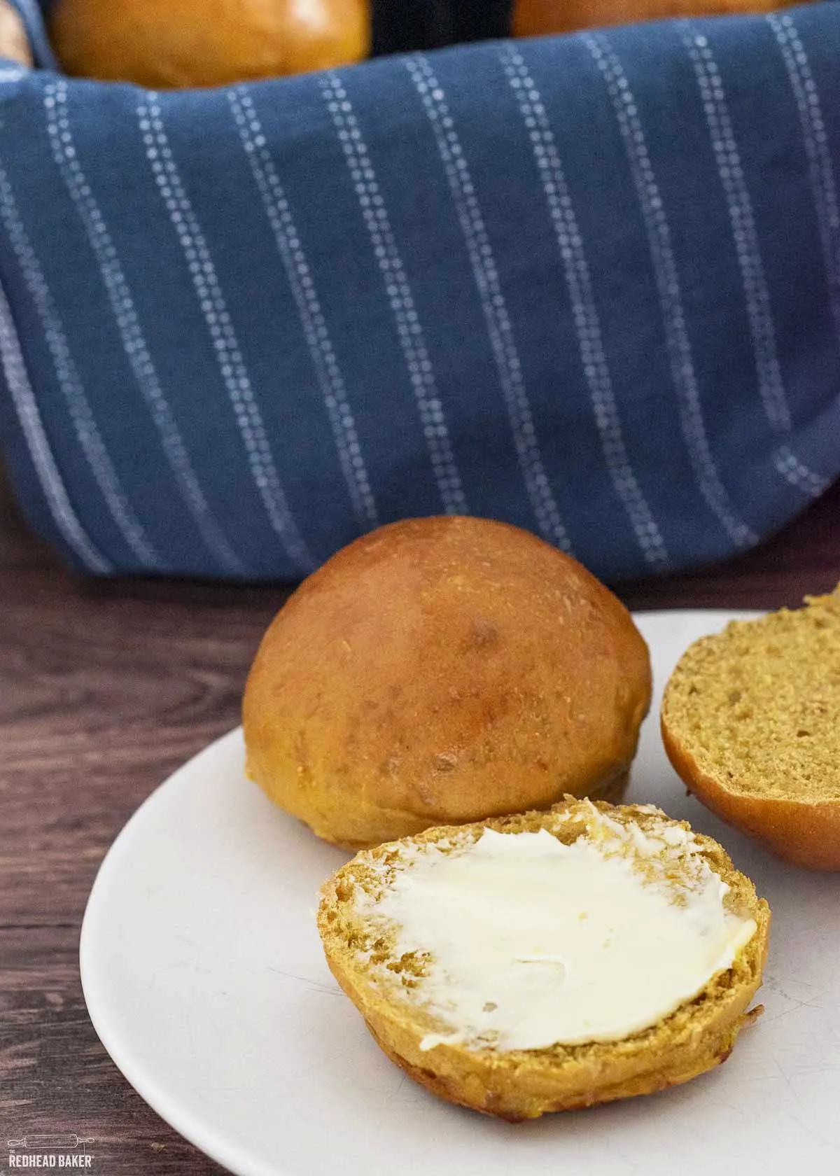 Two pumpkin rolls on a white plate, one split in half and buttered. 