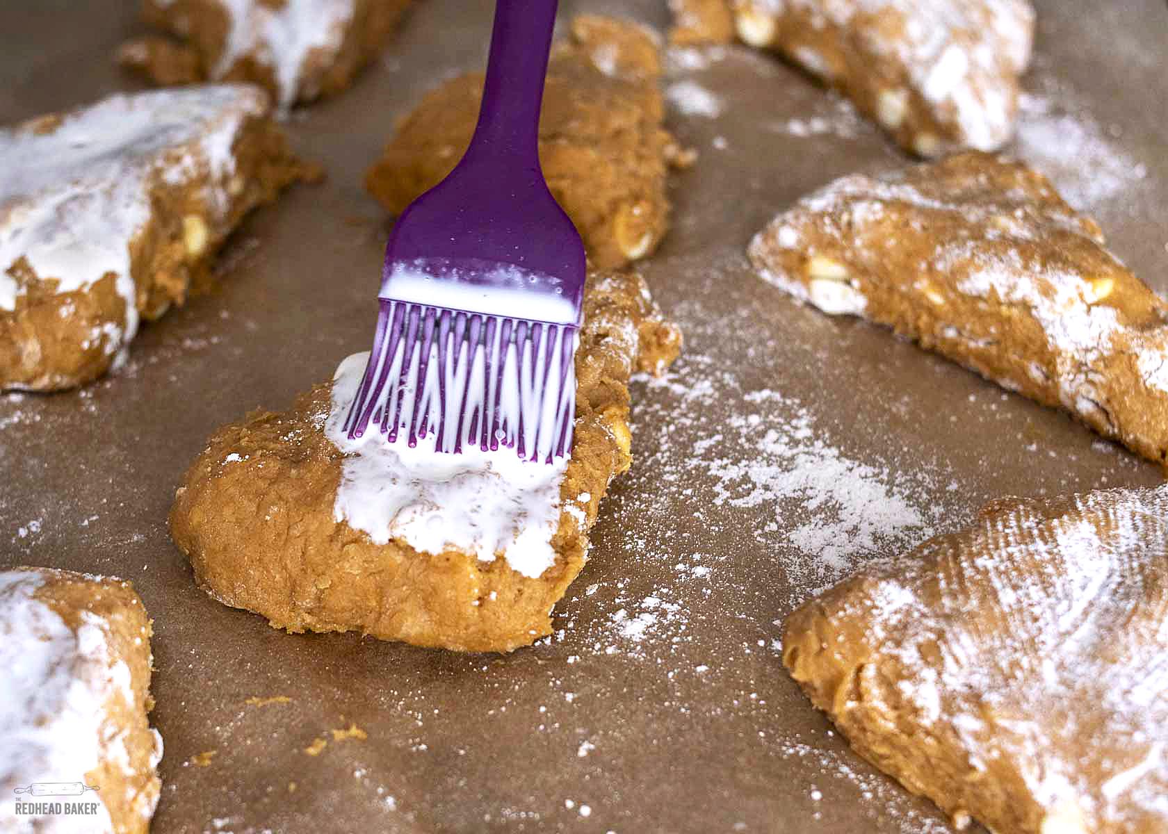 Cream being brushed onto a pumpkin scone. 