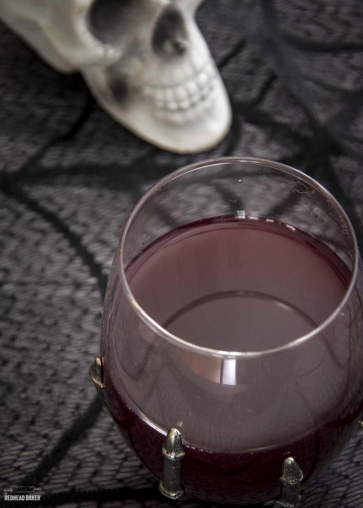 A glass of sangria in front of a plastic skull decoration. 