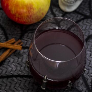 A glass of red cider sangria next to cinnamon sticks and a honeycrisp apple.