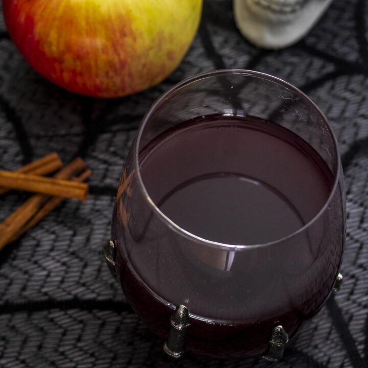 A glass of red cider sangria next to cinnamon sticks and a honeycrisp apple.