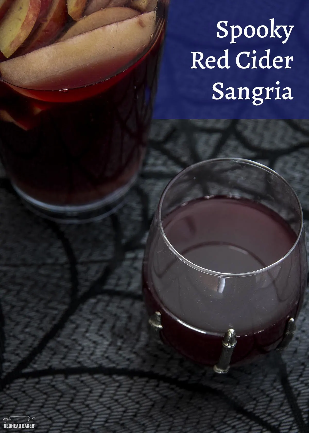 A glass of red cider sangria in front of a pitcher of sangria.